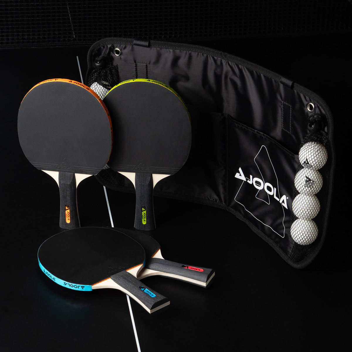 Four table tennis bats with coloured handles and a net with four white table tennis balls on a black background.