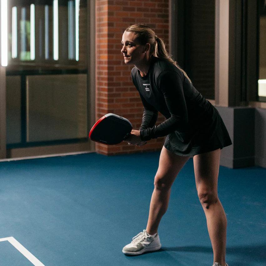 Woman in sports clothing holding a padel bat on an Indoor padel court.